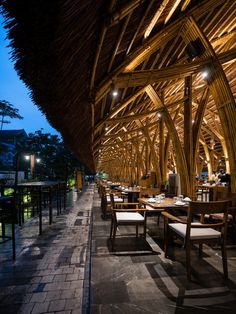 the inside of a restaurant with tables and chairs covered in straw roofing at night