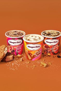 three cups of ice cream and cookies on an orange background with the words haagen - dees