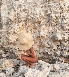 a woman sitting on rocks wearing a hat