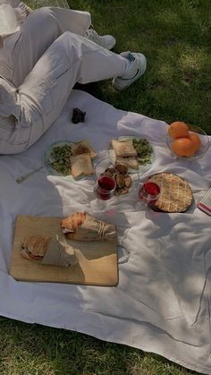 a person laying on the grass with food and drinks in front of them, including sandwiches