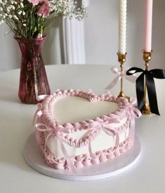 a pink heart shaped cake sitting on top of a table next to candles and flowers