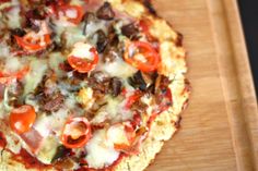 a pizza with cheese, tomatoes and other toppings sitting on a cutting board next to a knife