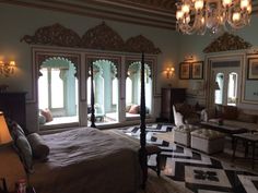 a large bedroom with chandelier, bed and couches in front of two windows