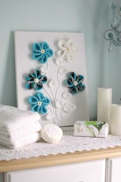 a white dresser topped with towels and flowers next to a wall mounted art piece on top of it