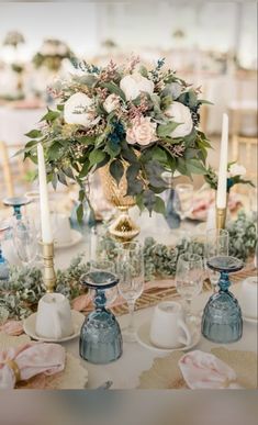 a table topped with lots of blue vases filled with flowers next to white candles