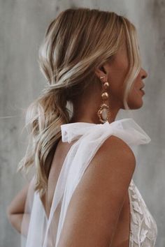 a woman with blonde hair wearing large gold earrings and a white dress is looking off to the side