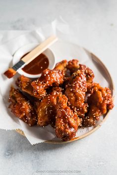 a white plate topped with wings covered in sesame seeds next to dipping sauce and a wooden spoon