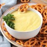 a bowl of dip surrounded by pretzels on a plate