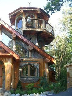 a house made out of wood and stone with a balcony on the second floor, surrounded by trees