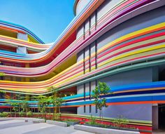 the colorful building has many windows and balconies on each floor, with trees in front of it