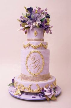 a purple and gold wedding cake with flowers on top