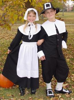 two children dressed as pilgrim and witch posing for the camera in front of a tree