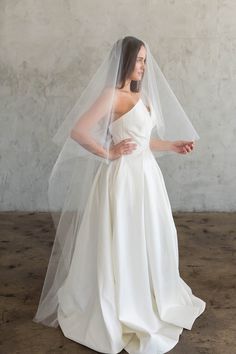 a woman in a white wedding dress with a veil on her head and hands behind her back