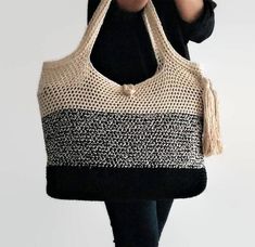 a woman carrying a black and white knitted tote bag with tassels