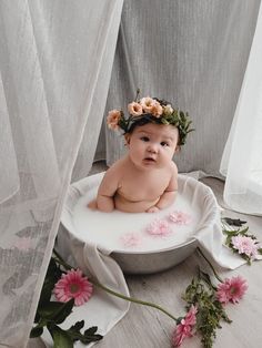 a baby is sitting in a bathtub with flowers on it's head and wearing a flower crown