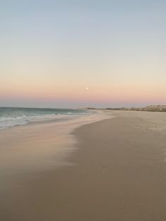 the sun is setting on the beach with waves in the foreground and sand dunes to the right