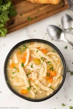 a bowl filled with chicken noodle soup next to some bread and parsley on the side