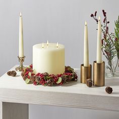 three candles are sitting on a table with pine cones and holly wreaths around them