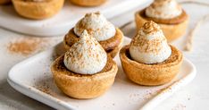 small desserts are sitting on white trays with cinnamon sprinkles and whipped cream