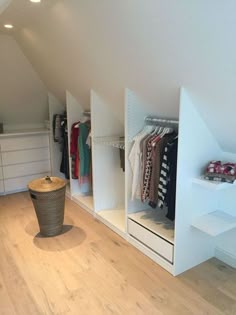 an attic bedroom with white shelving and clothes hanging on the walls, along with wooden floors