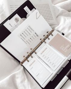 a black and white binder on top of a bed next to an open planner