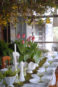 the table is set with white dishes and vases filled with red tulips