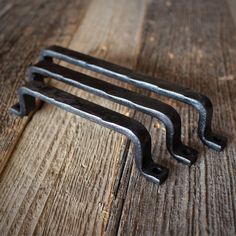 three metal handles are sitting on a wooden surface