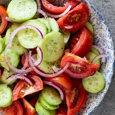 a blue and white bowl filled with cucumbers, onions, tomatoes and onion