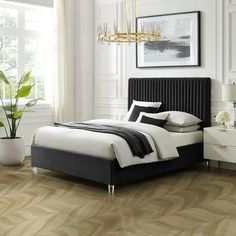 a bedroom with white walls and wood floors, a black headboard on the bed