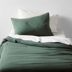 a bed with green sheets and pillows on top of it, next to a white wall