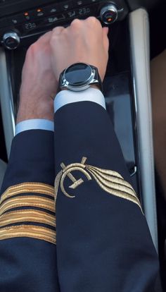 a man in uniform is driving a car with his hand on the steering wheel while wearing a watch