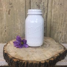 a white mason jar sitting on top of a tree stump next to a purple flower