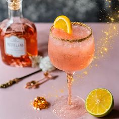 a pink drink with a lemon slice on the rim next to a bottle of booze