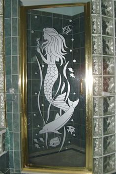 a bathroom with green tile and gold trim around the shower door, which has a mermaid design on it