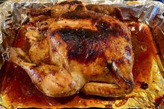 a roasted chicken on tin foil with sauce and seasoning in the pan, ready to be cooked