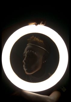 a person holding a circular light up in the dark with their face reflected in it