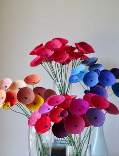 a vase filled with colorful paper flowers on top of a wooden table next to a white wall