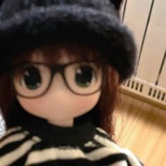 a close up of a doll wearing glasses and a striped shirt with a black hat