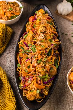 a bowl filled with noodles and vegetables on top of a wooden table next to other bowls