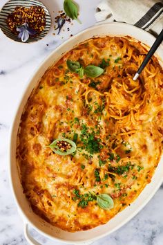 a casserole dish with spaghetti and parsley in it on a marble table