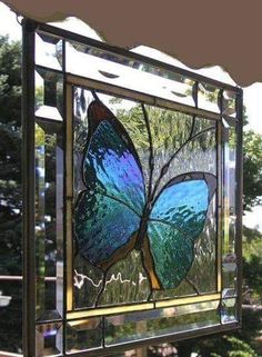 a stained glass window with a blue butterfly on it's side and trees in the background