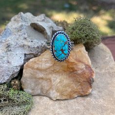 An oval shaped #8 turquoise stone is wrapped in fine silver and surrounded by a tightly twisted silver rope. This stone I would describe as a teal blue with beautiful matrix.  The head of this ring measures 1/2" wide x 3/4" long. Please see photos for size reference.  The ring band is made of sterling silver and has a plain and smooth center with textured edges.  Size: 7-1/2 * This ring cannot be resized  All photos are taken in natural outdoor lighting conditions. Please contact me with questions or for additional photos Ring Band, Turquoise Stone, Solitaire Ring, Fine Silver, Teal Blue, Oval Shape, Matrix, Outdoor Lighting, Band Rings