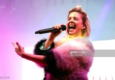 a woman singing into a microphone while holding her hands out to the side with one hand