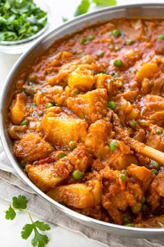 a pan filled with chicken curry and garnished with cilantro on the side