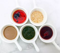 six different sauces in small white bowls on a marble surface