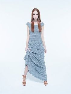 a woman with long red hair wearing a blue dress and brown sandals standing in front of a white background