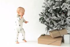 a baby standing in front of a christmas tree with presents on the ground next to it