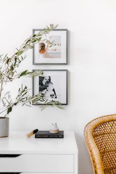 two framed pictures hang on the wall above a white desk with a wicker chair