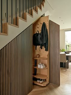 an open closet with shoes and coat hanging on the wall next to a stair case