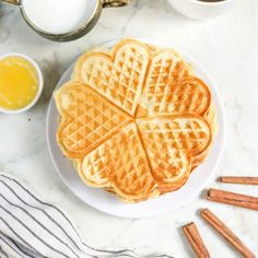 a white plate topped with waffles next to two cups of orange juice and cinnamon sticks